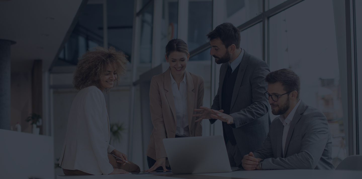 Quatre professionnels en tenue de bureau discutent autour d'un ordinateur portable dans un bureau moderne et lumineux.