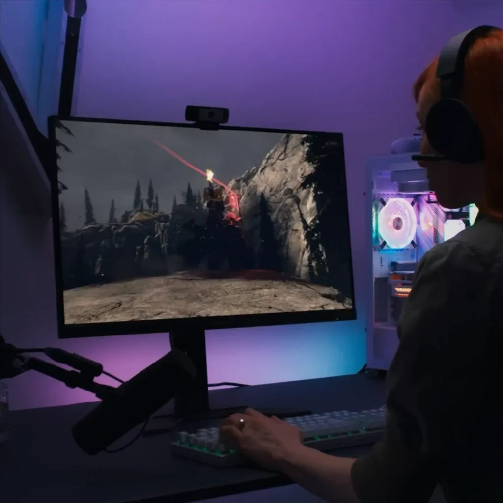 Une personne avec casque joue sur un grand écran, assise à un bureau éclairé de lumières violettes et bleues, PC gamer Windows 11 Pro à côté.