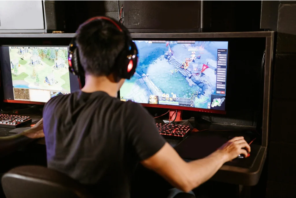 Une personne avec un casque joue à un jeu vidéo sur un grand écran incurvé, clavier visible, idéal pour tester Windows 11 Home vs Pro.
