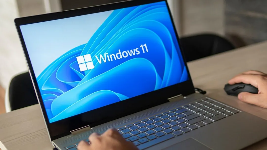 Un utilisateur travaille sur un ordinateur portable Windows 11 Pro + Office 2024, logo visible sur écran bleu, main sur la souris.