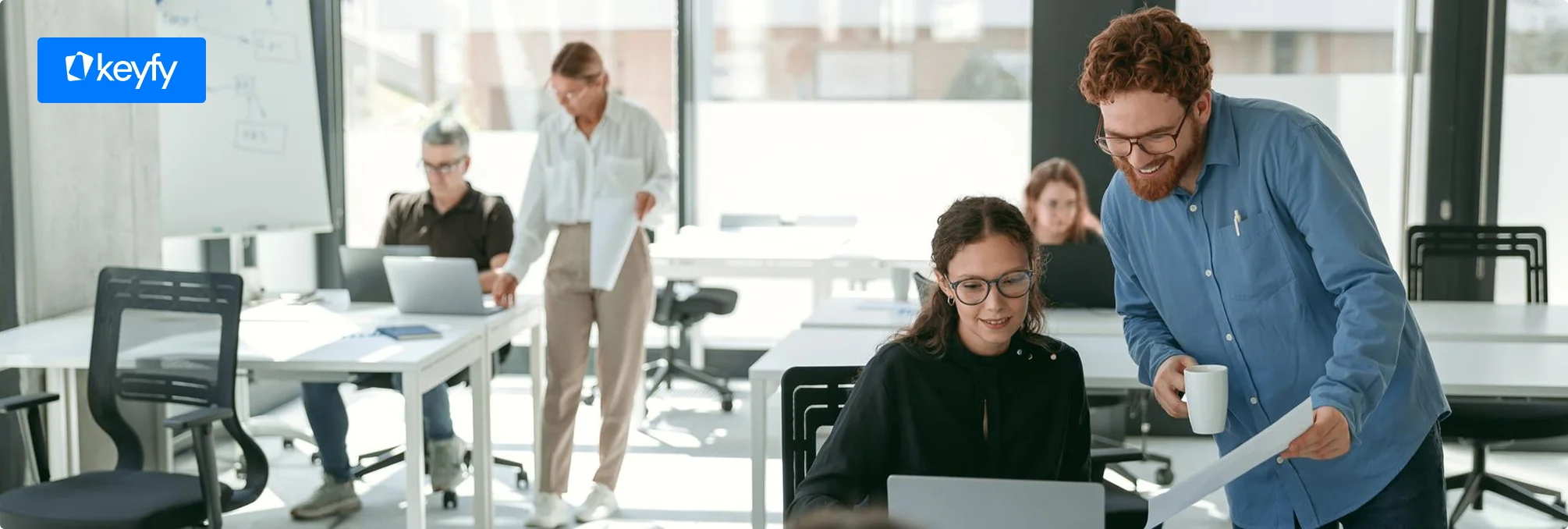 Bureau moderne avec cinq personnes : deux collaborent sur un ordinateur portable, trois travaillent seules. Logo Keyfy en haut à gauche.