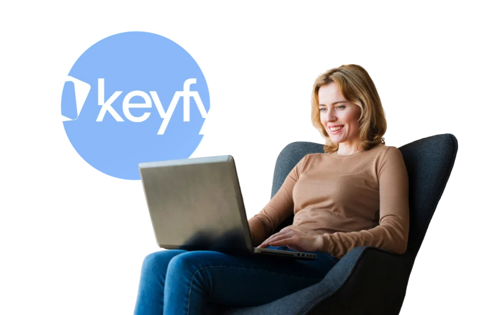 Une femme assise confortablement sur une chaise sourit en utilisant un ordinateur portable, à côté du logo bleu keyfy.