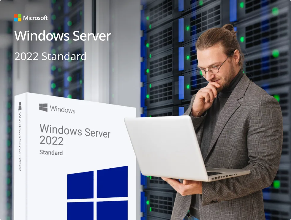 Un homme en costume gris travaille sur un ordinateur portable dans une salle serveur, devant une boîte Windows Server 2022 Standard.