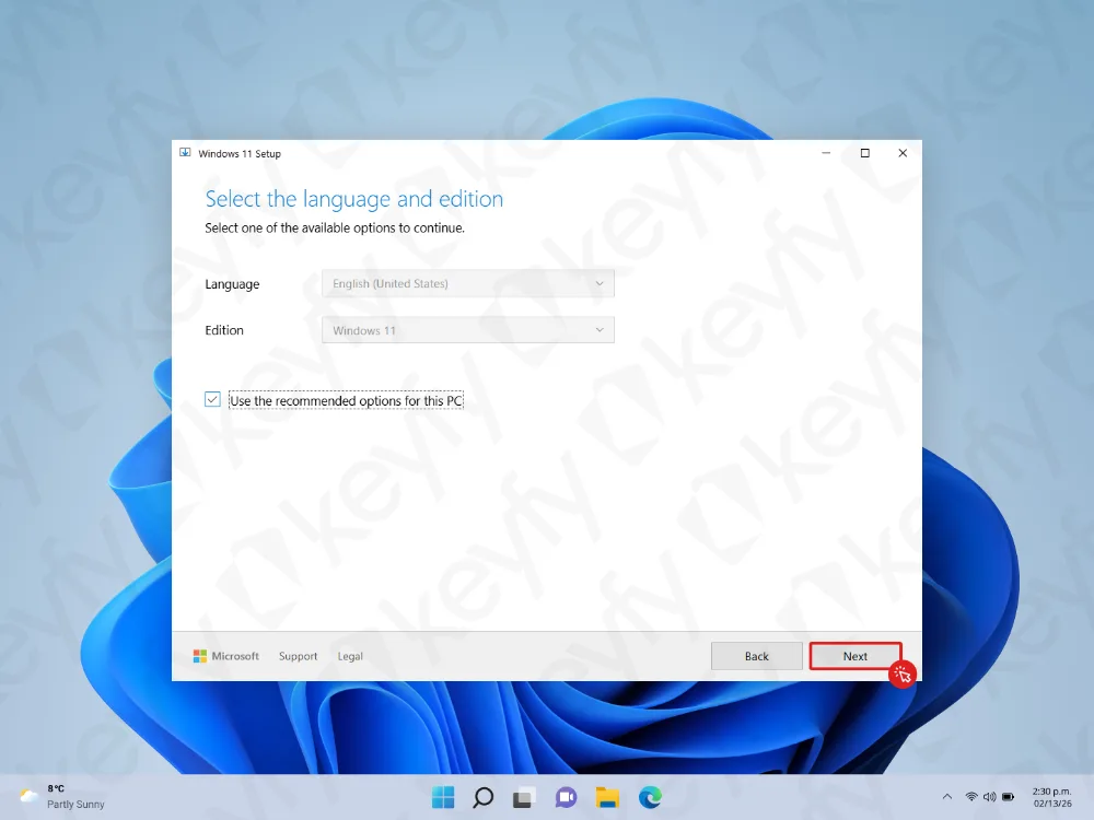 Un écran de configuration de Windows 11 invitant l'utilisateur à sélectionner la langue et l'édition. Le bouton « Suivant » est mis en évidence en rouge en bas à droite. L'arrière-plan de l'écran montre le fond d'écran et la barre des tâches par défaut de Windows 11.
