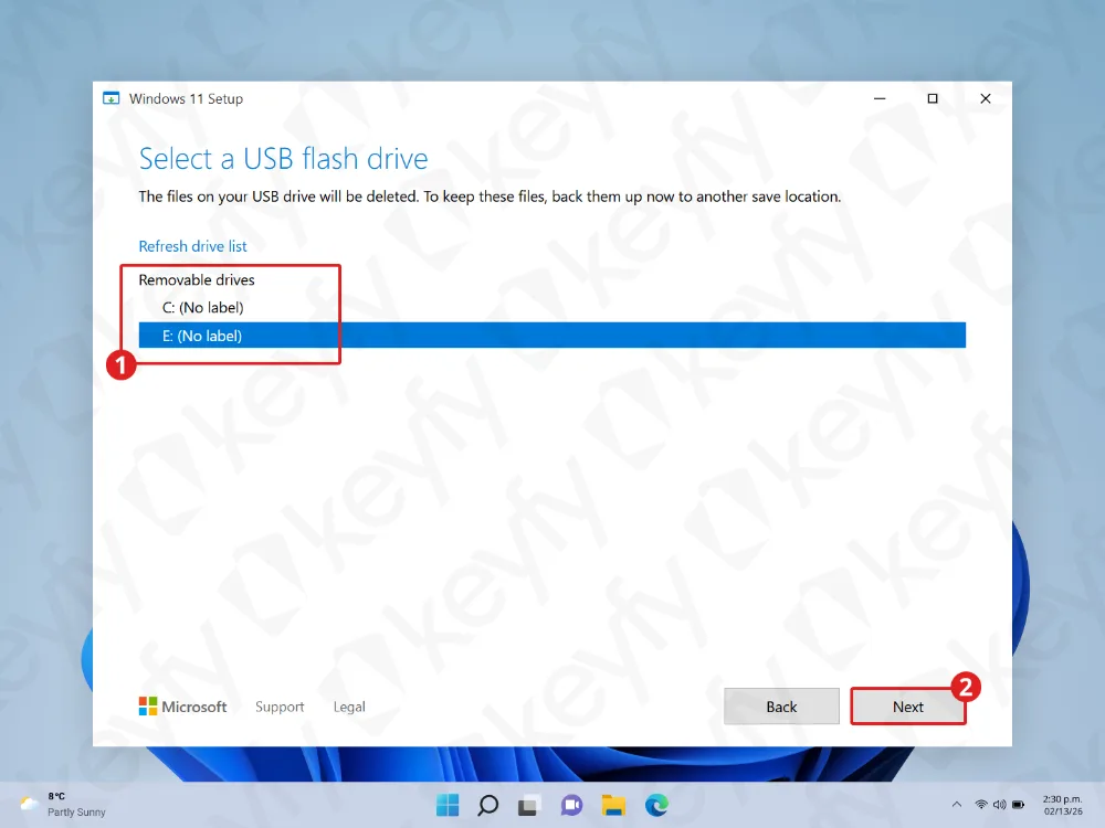 Un écran de configuration de Windows 11 affichant deux lecteurs amovibles, C: et E:, avec E: sélectionné. Le bouton Suivant en bas à droite est mis en évidence, et l'arrière-plan du bureau est visible derrière la fenêtre de configuration.